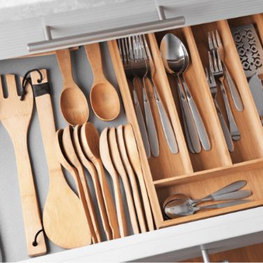 An organized kitchen drawer with wooden spoons, spatulas, and cutlery including forks, spoons, and knives, all neatly arranged in a bamboo utensil tray.