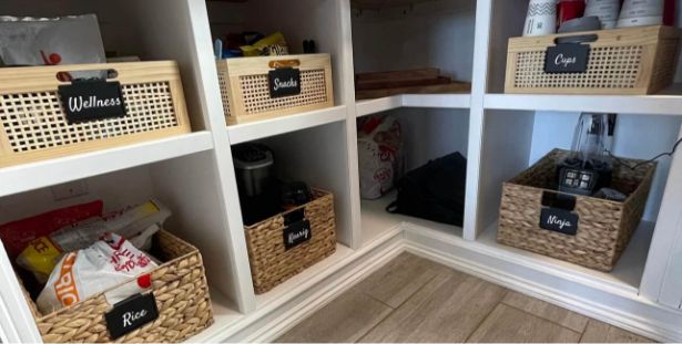 A neatly organized pantry with labeled baskets for Wellness, Snacks, Rice, Cups, and Mojo. The shelves are white, and the baskets—reminiscent of the thoughtfully curated Mega Menu on our website—are a mix of wicker and wood, holding various food items and kitchen supplies.