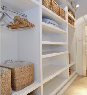 A modern walk-in closet with white shelves, wooden hangers on a metal rail, and several woven baskets neatly arranged on shelves and the floor. The space is well-lit and organized, offering services akin to a mega menu of storage solutions to keep your wardrobe seamlessly managed.