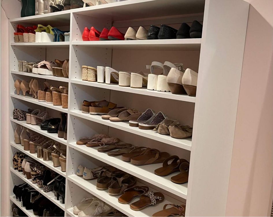 White shelves filled with neatly organized women’s shoes, including high heels, wedges, sandals, and flats in various colors and styles. The shoes are arranged in rows by type and color.